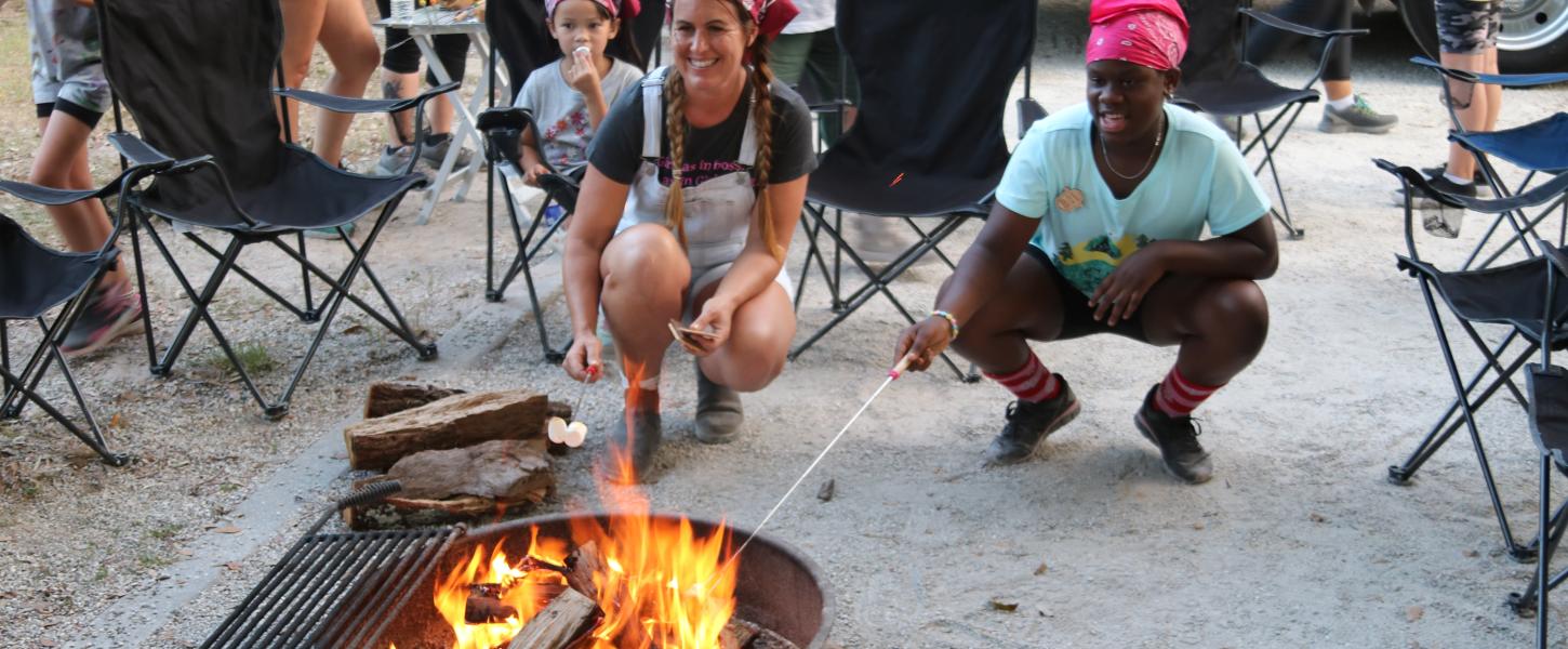 Two Girl Scouts roast marshmallows over a campfire.