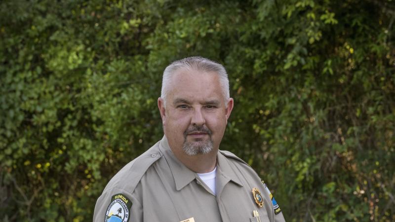 A park ranger in class A uniform posing in front of greenery