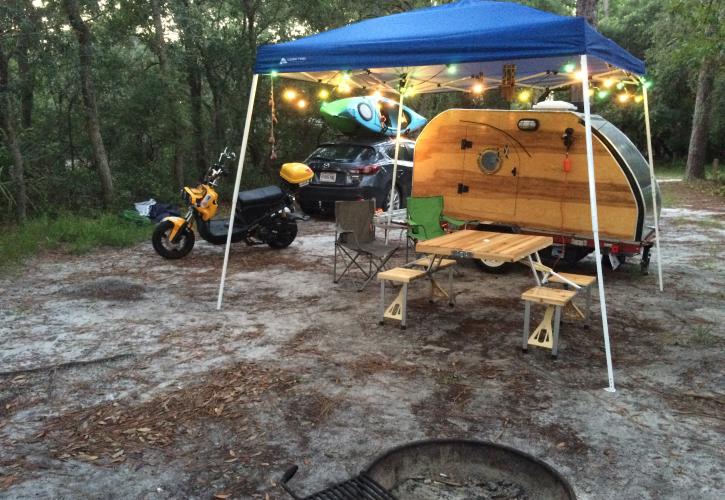 Tear drop camper set up under pop up tent next to motorcycle.