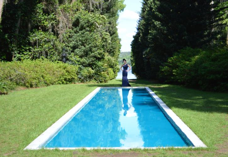 Girl in gown stands on far end of blue waters of reflection pond.