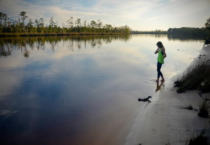 Girl wades at waters edge in ankle deep water.